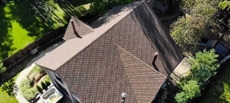 A roofer examines damaged shingles and flashing on a residential roof while reviewing notes with a homeowner.